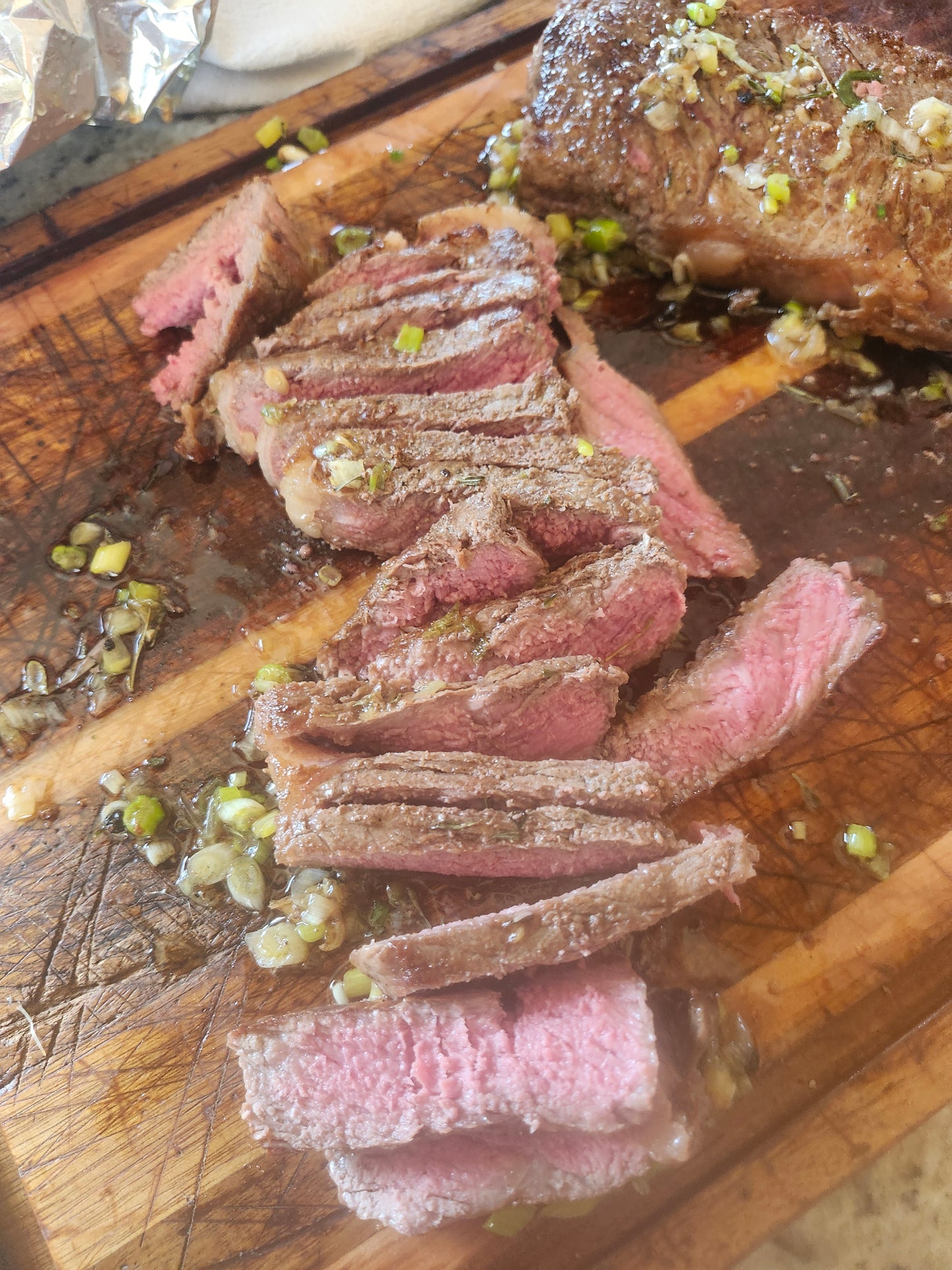 Sliced NY Strip steak bennion beef on cutting board with green onion and olive oil